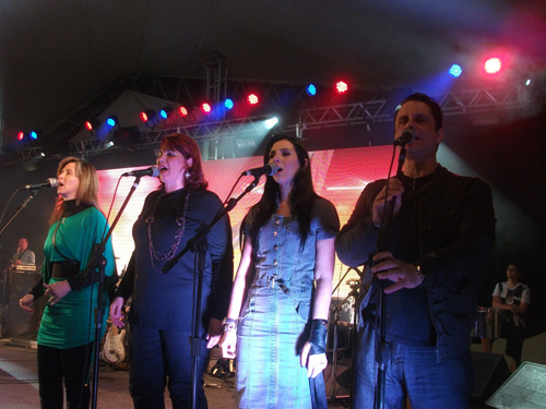 Vocalistas no palco com luzes coloridas ao fundo