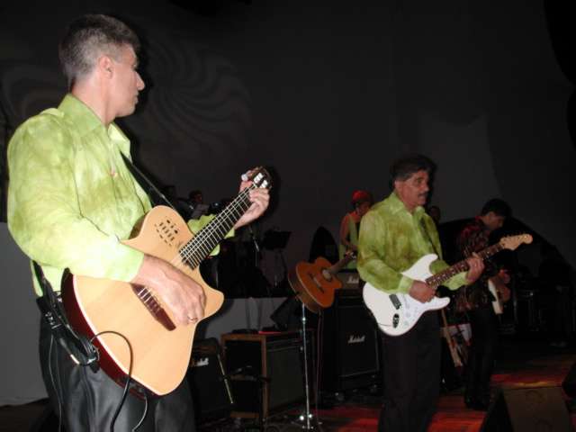 Violonista em primeiro plano e guitarristas ao fundo