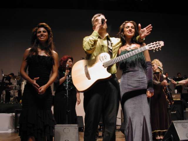 Apresentação musical no palco com violonista e cantoras
